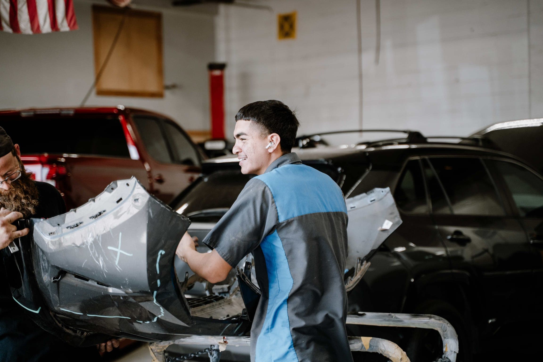 Auto body technicians carrying a vehicle bumper cover through a collision repair shop